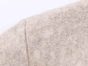 Dettaglio della cucitura sulla spalla in maglia beige e trama della giacca con cappuccio