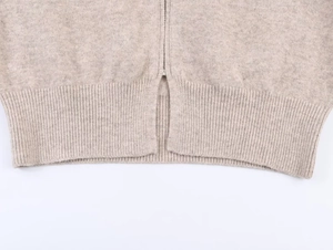 Dettaglio dell'orlo a coste e della cerniera metallica sul cardigan in maglia beige