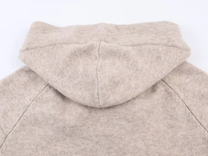 Dettaglio del cappuccio in maglia beige con focus su cuciture e trama del materiale