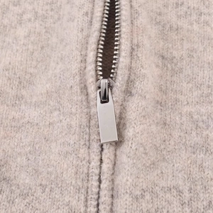 Dettaglio della felpa in maglia con cerniera in metallo argento su tessuto grigio chiaro