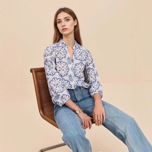 Detail of blue geometric floral print on women's white blouse with gold bracelet