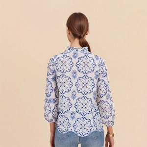 Detail of blue floral embroidery on white blouse with ruffled collar and scalloped hem