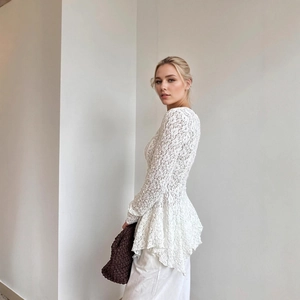 Detail of elegant white lace top showing asymmetrical peplum hem and floral texture