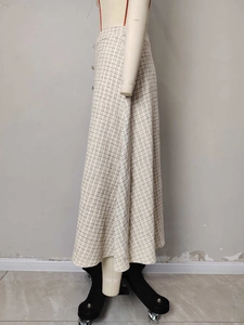 Detail van een crèmekleurige tweed A-lijn rok met metalen knoop en geruit patroon