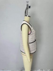 Detail of light beige quilted vest with black scalloped trim and side pocket on mannequin