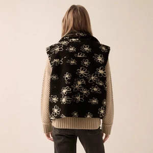 Back view of a black floral fleece vest layered over a beige chunky knit sweater