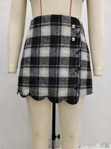 Detail of black and white plaid mini skirt with wavy hem and golden embossed buttons