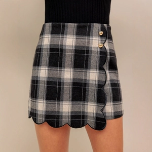 Detail view of high-waist plaid skirt with scalloped hem and decorative gold metal buttons