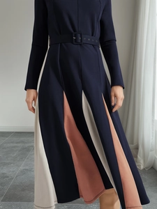 Detail view of long-sleeved A-line dress with color-block pleated skirt and waist belt