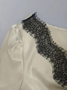 Detail eines cremefarbenen Satin-Kleids mit schwarzer Wimpernspitze und plissiertem Puffärmel