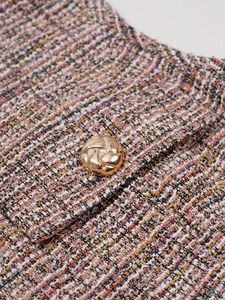 Détail du tissu tweed coloré avec un bouton en métal doré sur un gilet chic