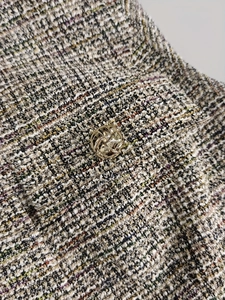 Gros plan sur la texture du tweed multicolore et le détail d'un bouton doré en métal