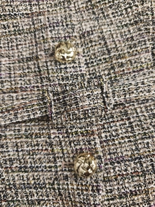 Détail de la texture en tweed avec boutons en métal doré et boucle en tissu assortie