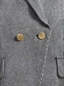 Detail of grey houndstooth blazer showing golden metallic buttons and woven fabric texture