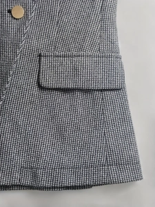 Detail shot of grey houndstooth blazer featuring golden buttons and flap pocket texture