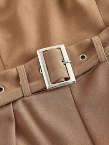 Close-up of tan jumpsuit waist with silver buckle belt and detailed fabric texture