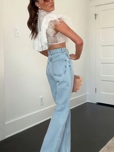 Detail view of white lace sheer top with ruffled mesh layers and high-waist jeans