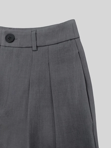 Detailed close-up of charcoal grey trouser waist with pleats and polished button