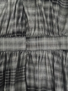 Detail van geruite jurk met tailleplooien en geweven textuur van de geruite stof