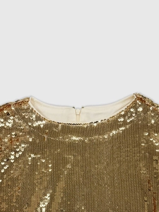 Detail showing the golden sequin texture with a round neckline and hidden back zipper