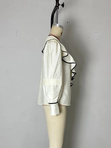 Détail latéral de la blouse crème à col en V avec bordures ondulées noires contrastées