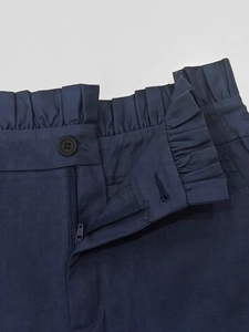 Detail of high waist navy shorts featuring ruffled paperbag waist and metal button