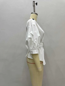 Dettaglio di camicia bianca con scollo a barca, maniche a sbuffo, cintura e bottoni laterali
