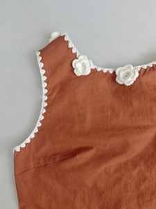 Dettaglio di abito rosso-marrone con pizzo all'uncinetto bianco e fiori fatti a mano