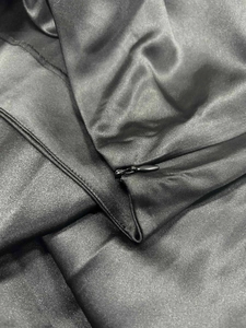 Detailed macro view of the invisible zipper closure on a black satin midi skirt