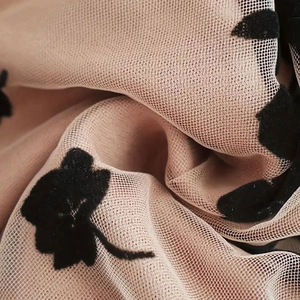 Detailed macro view of beige mesh fabric featuring 3D black flocked floral patterns