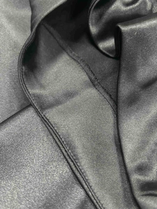 Detailed macro view showing the smooth black satin fabric and flat seam stitching of the skirt