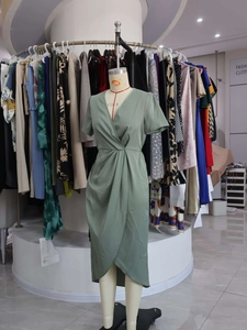 Detail of sage green wrap dress showing V-neck design and twisted waist knot on a mannequin