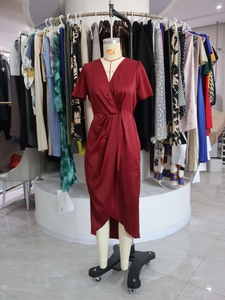 Detail of burgundy satin wrap dress with waist pleats and asymmetrical slit hemline