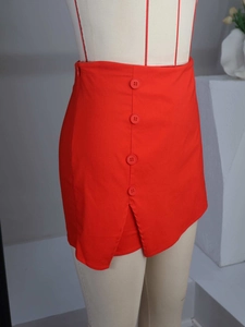 Detail view of red mini skort featuring decorative buttons and a side slit on the hemline