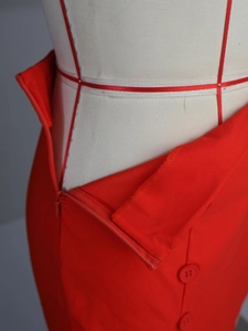 Detail of red high-waisted skirt featuring a hidden zipper and decorative buttons