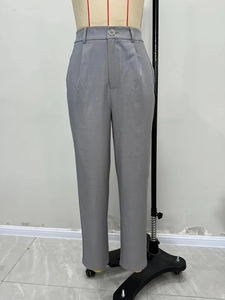 Dettaglio dei pantaloni da completo grigi a vita alta con bottone in metallo e tessuto