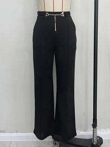 Detailed close-up of high-waist black wide-leg trousers with gold metal chain belt and tassel