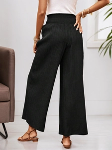 Detail of high waist smocked elastic waistband on black pleated wide-leg trousers