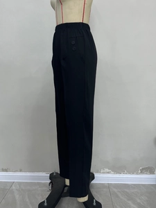 Detail view of high waisted black trousers with elastic waist and side decorative buttons