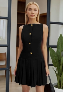 Detail of black sleeveless mini dress featuring gold geometric buttons and pleated skirt