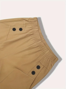 Detailed macro view of khaki plaid trousers showing elastic waist and decorative buttons