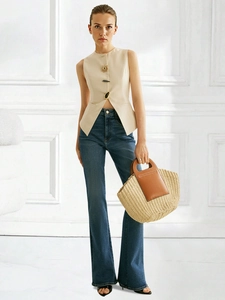 Detail of a beige sleeveless vest with gold buttons paired with blue flare jeans