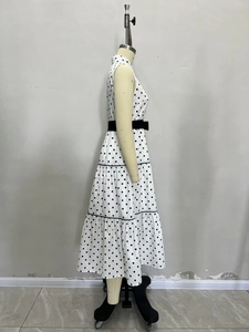 Dettaglio di un vestito a pois bianco senza maniche con gonna a balze e cintura nera