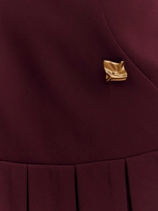 Detail of burgundy dress featuring a gold wavy buckle and sharp pleated fabric texture