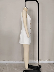 Détail d'une mini robe blanche sans manches ornée de boutons dorés en relief sur le devant