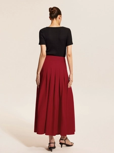 Back view of a woman wearing a black sleeveless top and red pleated midi skirt set