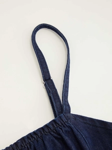 Dettaglio di spallina in denim blu scuro con fibbia in metallo argento e pieghe morbide