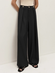 Detail of high waisted black trousers with golden vintage buttons and pleats