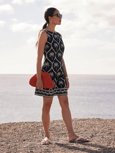 Ärmelloses marineblaues Kleid mit Palmenstickerei und orangefarbener Clutch am Strand