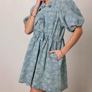 Detail of light blue puff sleeve dress with floral pattern and bow tie front design